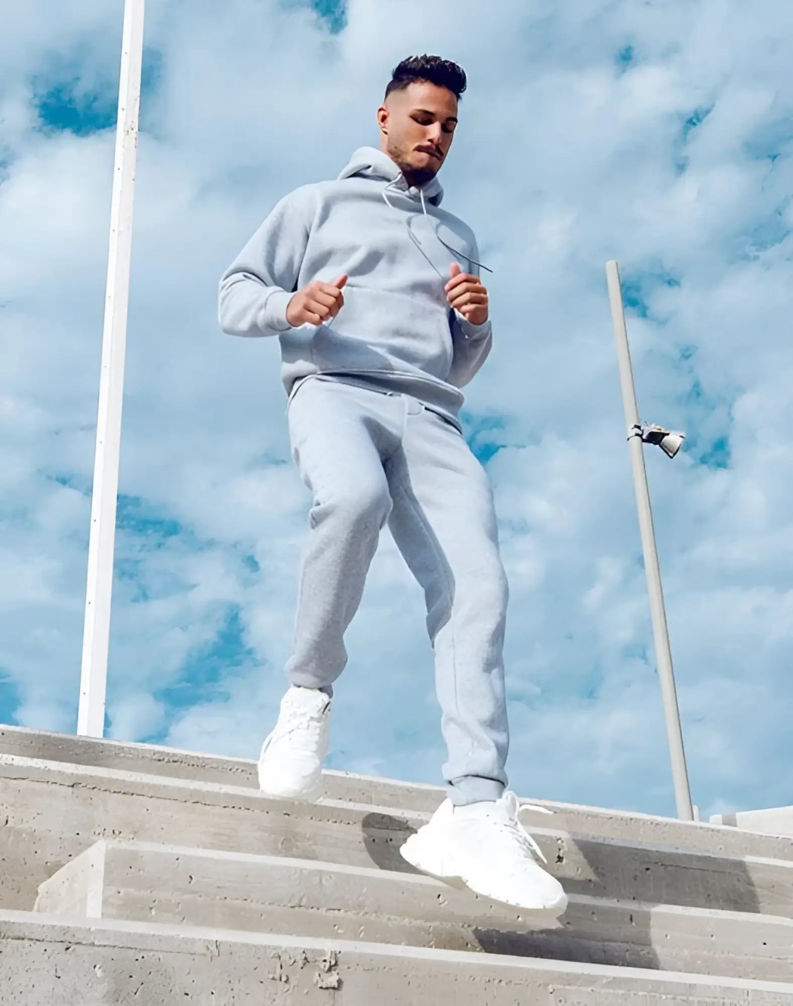 A man wearing light gray SUPAWEAR recovery pants and matching hooded sweatshirt made of comfortable fabric