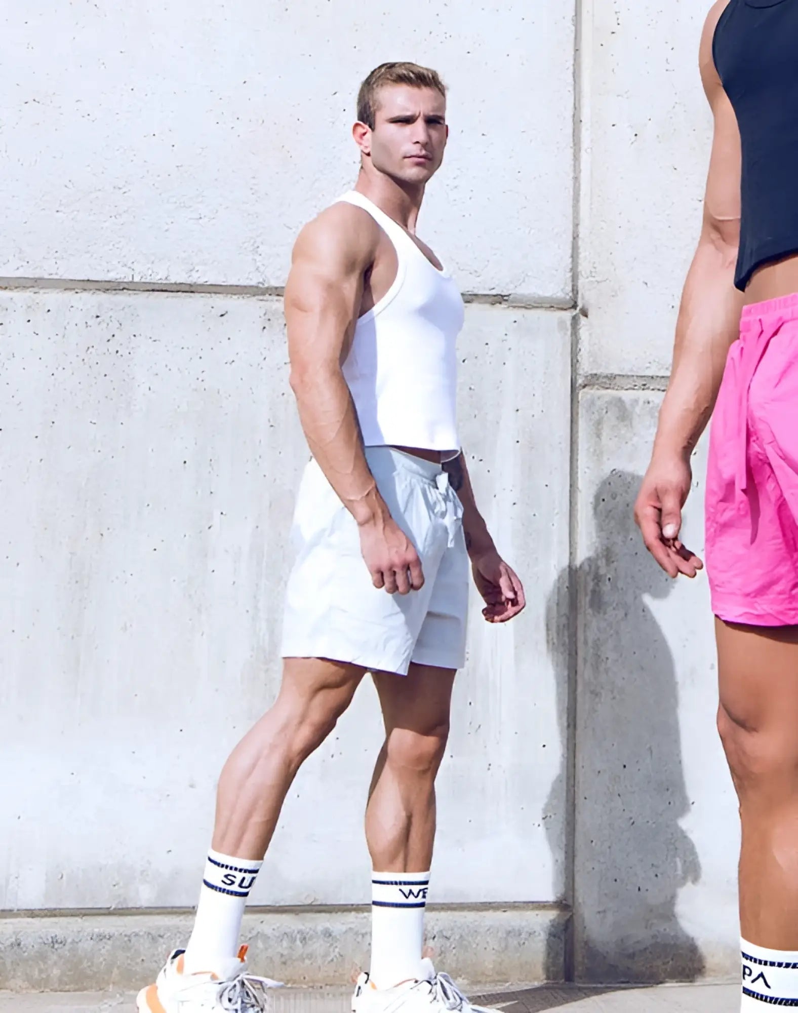 A man wearing a supawear ribbed cropped singlet in white paired with light gray shorts is shown from the front