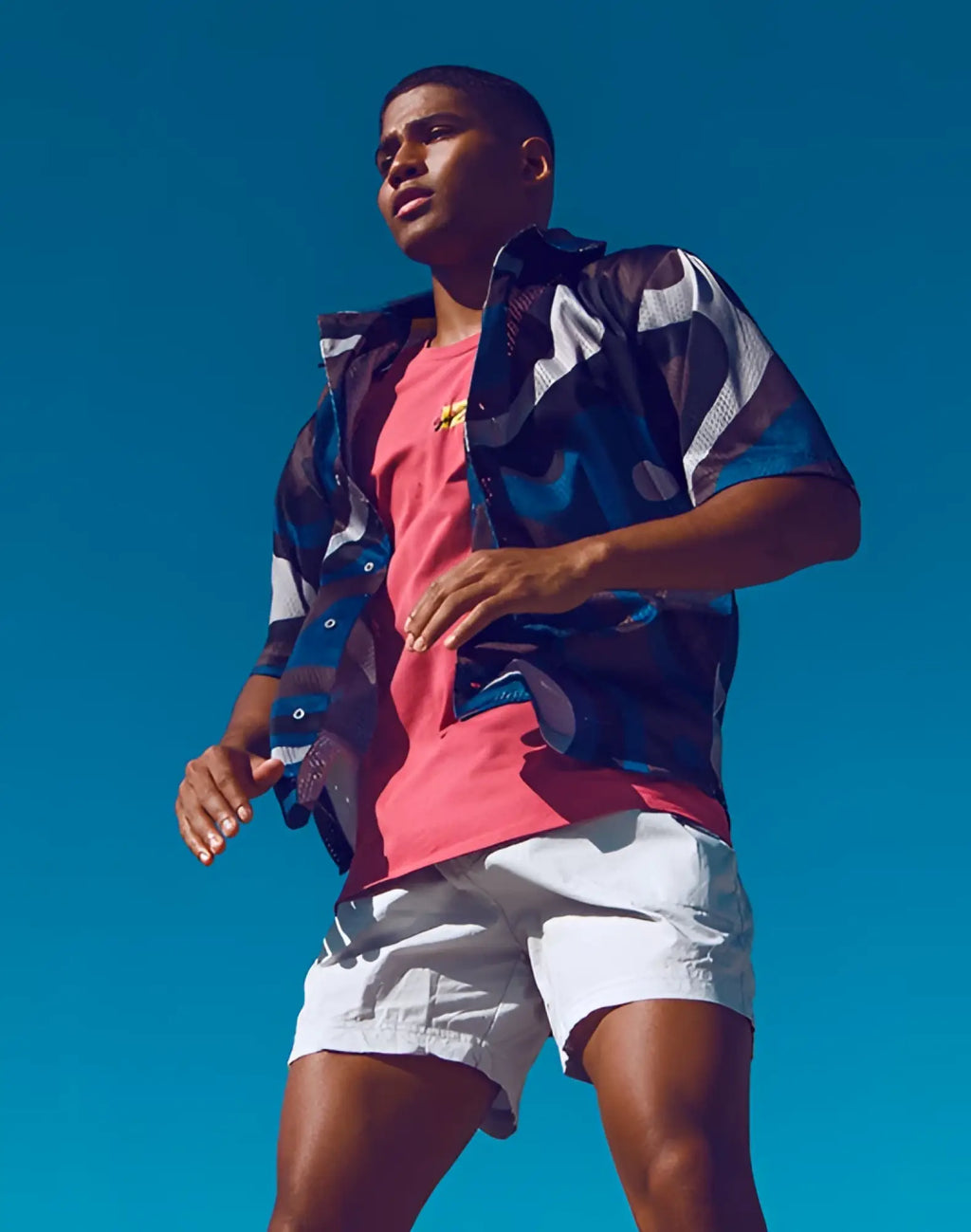 Man wearing a supawear short sleeve mesh shirt in blue combo print over a pink t-shirt with abstract designs