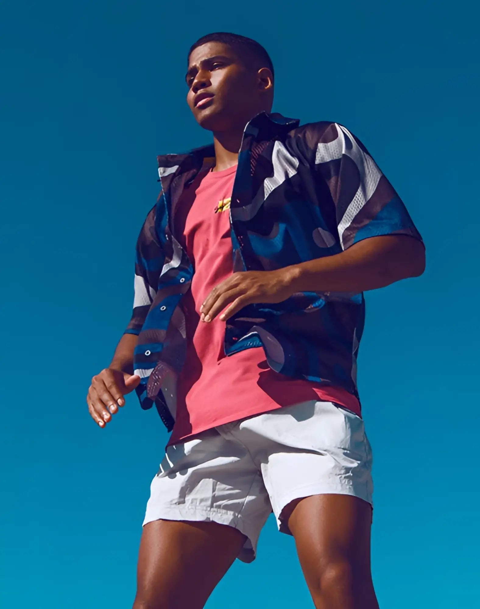 Man wearing a supawear short sleeve mesh shirt in blue combo print over a pink t-shirt with abstract designs