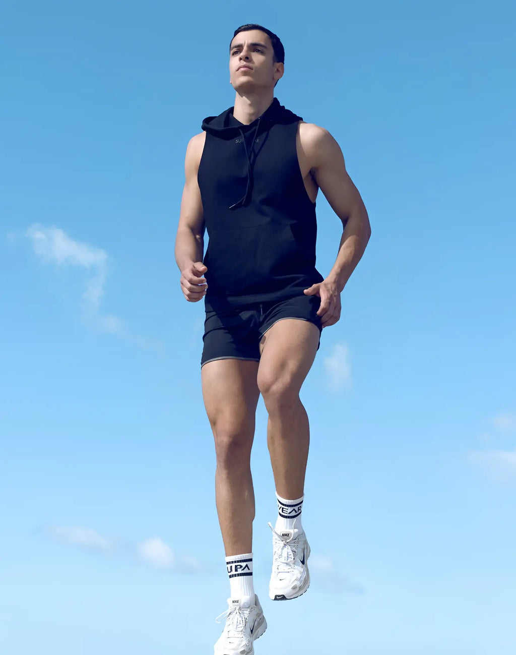 A man wearing a black sleeveless hoodie with drawstrings from supawear paired with black shorts white socks and sneakers