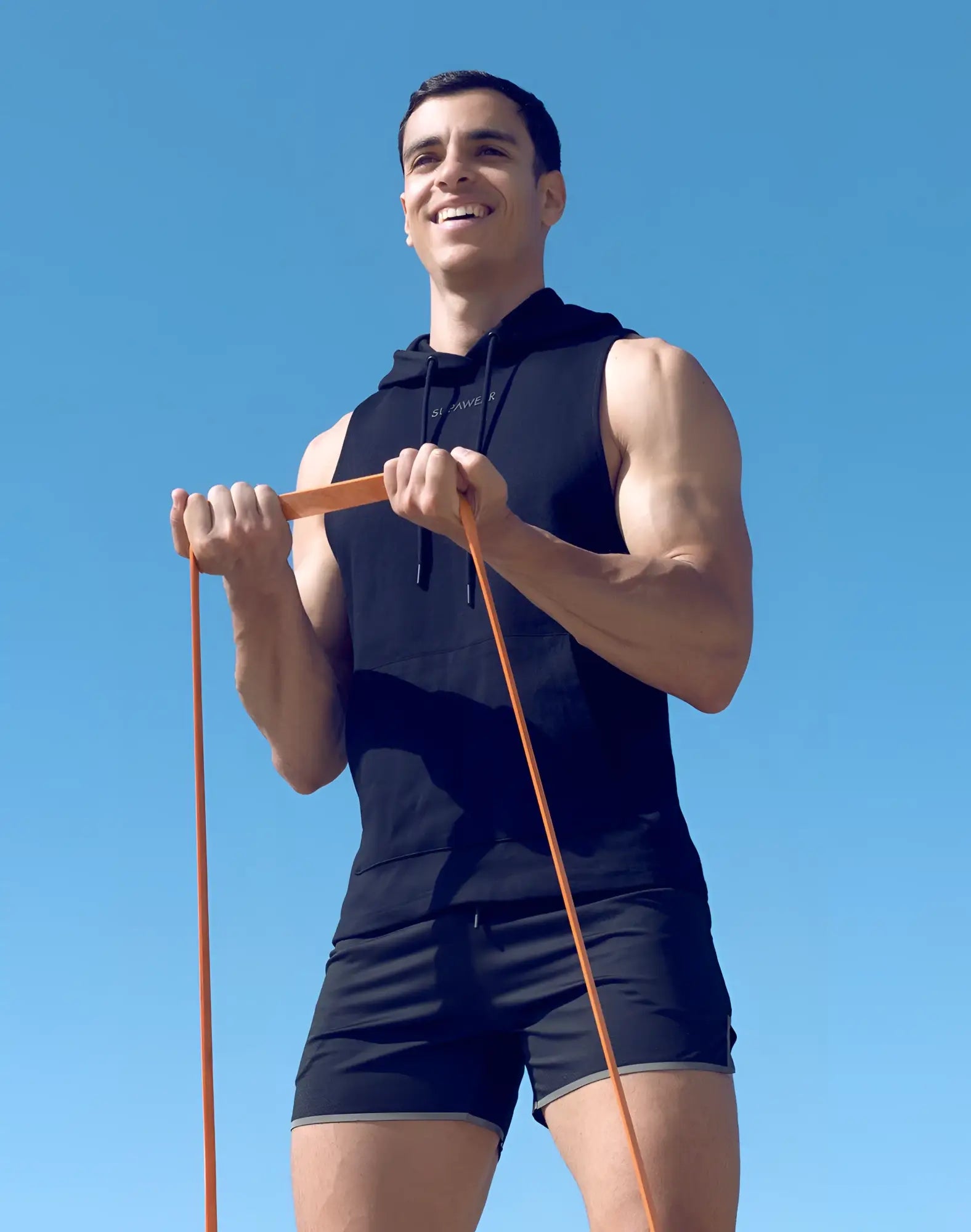Man in black wearing supawear sleeveless hoodie holding an orange resistance band for fitness workouts