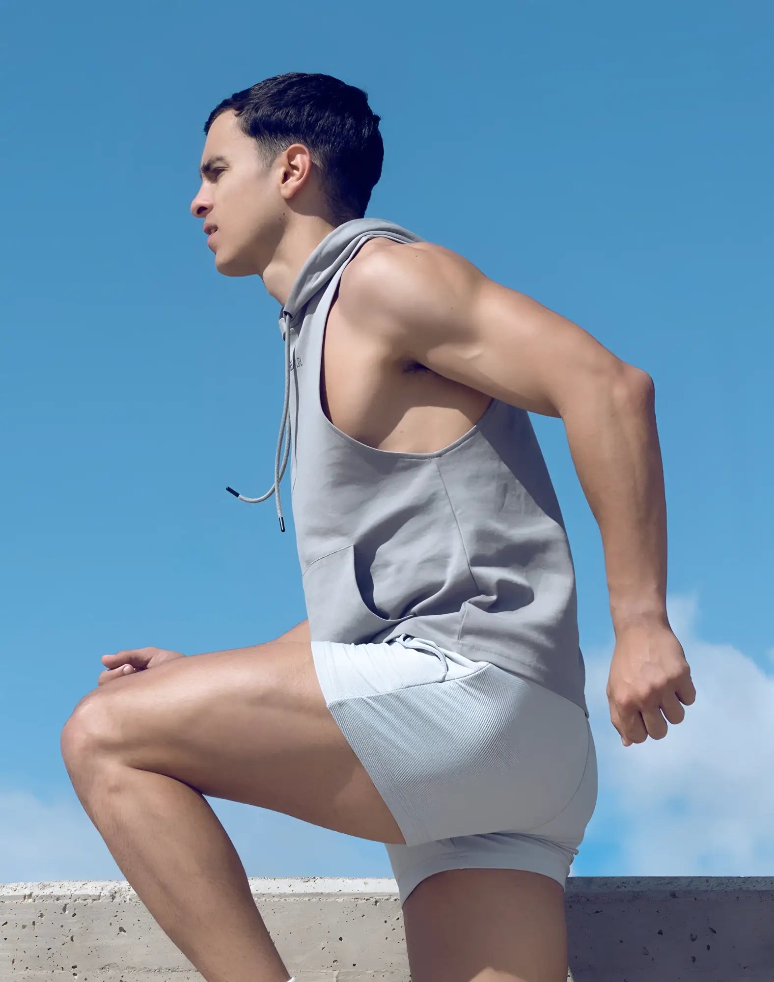 A man wearing a gray sleeveless hoodie with drawstrings and matching light gray athletic shorts from SUPAWEAR