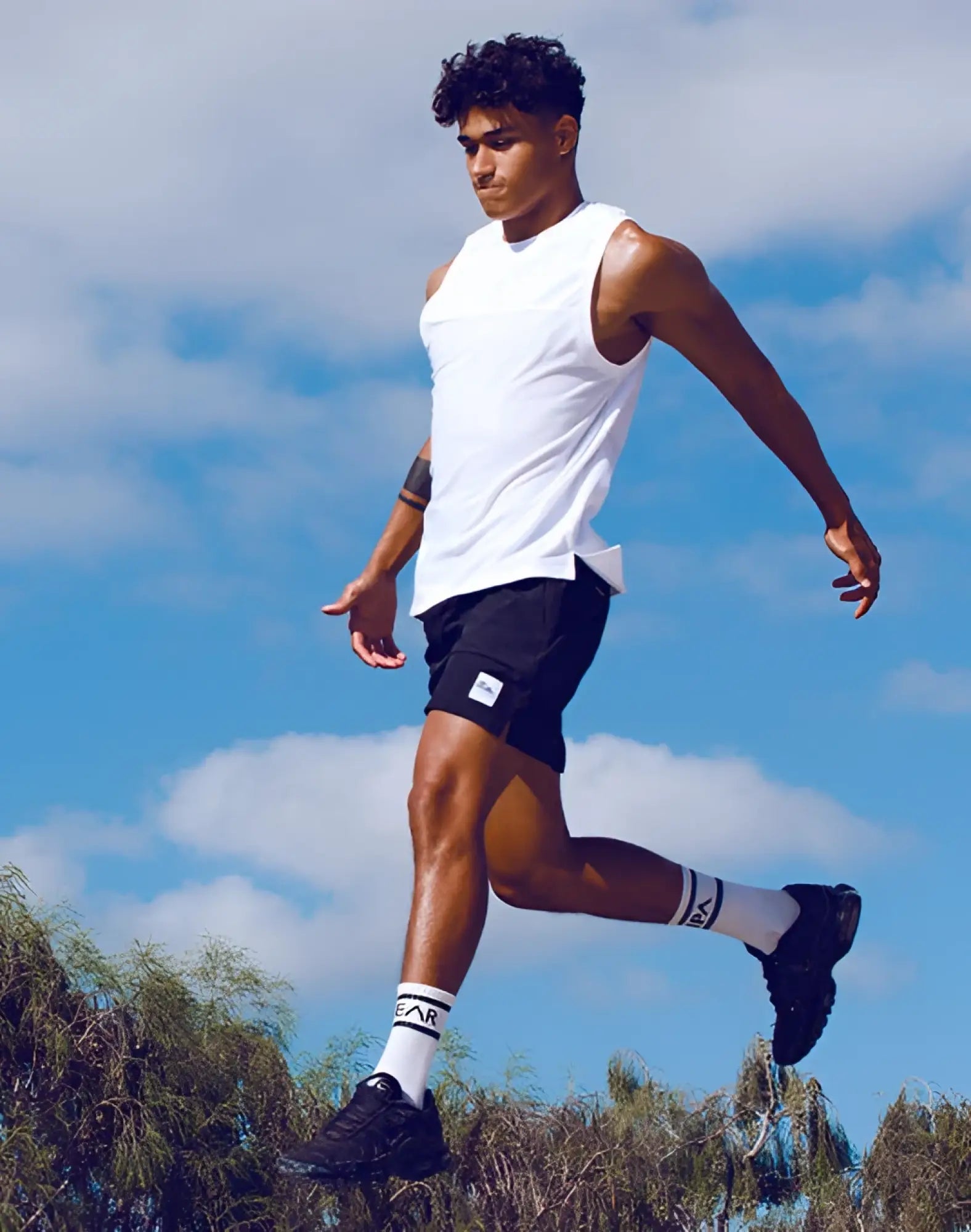 A man wearing a supawear solid and mesh white tanktop with black shorts featuring a small logo on the left leg