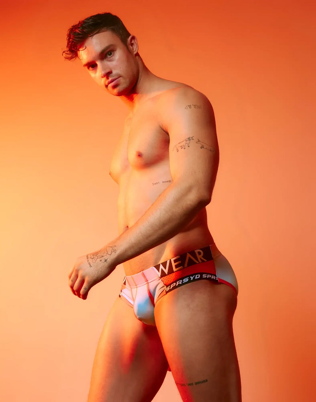 A man wearing supawear spr performance gradient brief underwear in rainbow colors with bold black and red waistband branding
