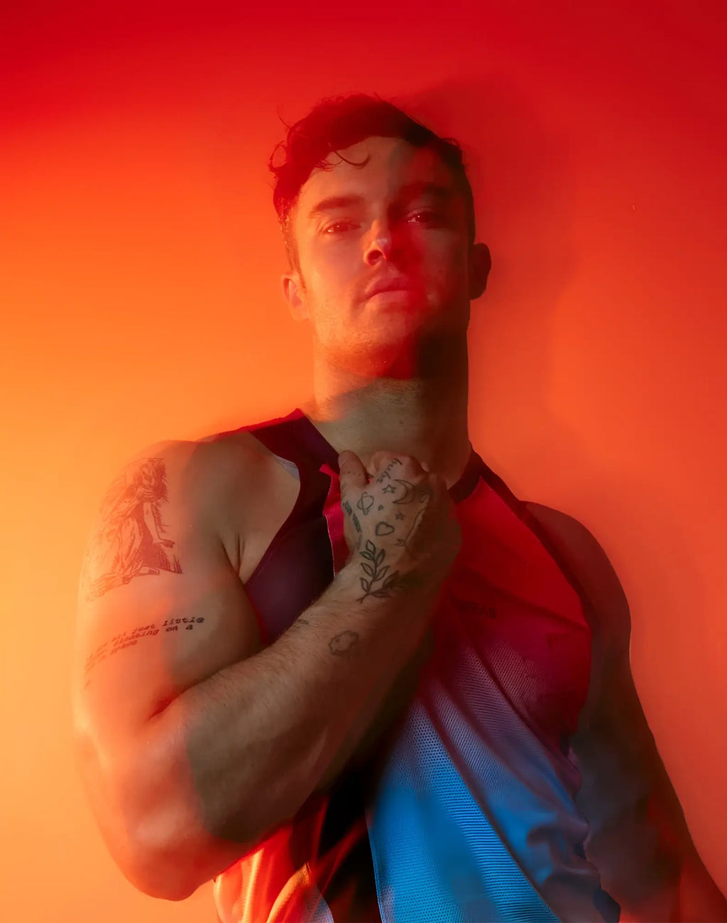 A man with tattoos wearing a sleeveless dark fabric supawear spr performance gradient singlet rainbow