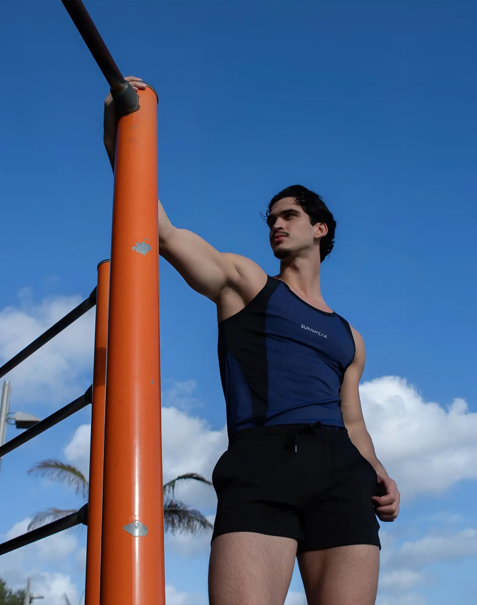 A man wearing a SUPAWEAR SPR performance singlet in navy blue and black with survivor print, paired with black shorts