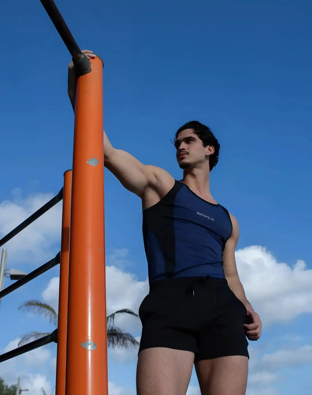 A man wearing a SUPAWEAR SPR performance singlet in navy blue and black with survivor print, paired with black shorts