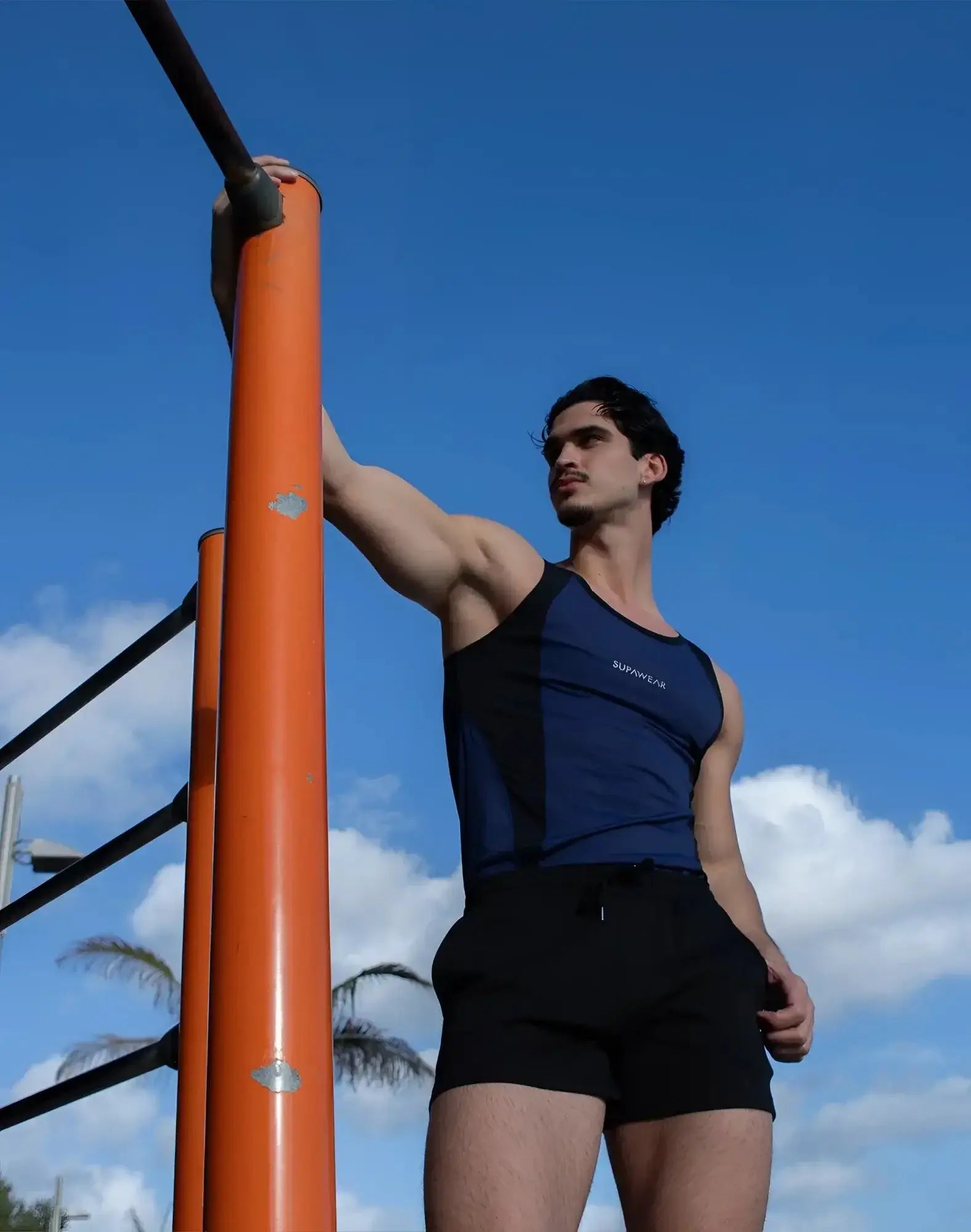 A man wearing a SUPAWEAR SPR performance singlet in navy blue and black with survivor print, paired with black shorts