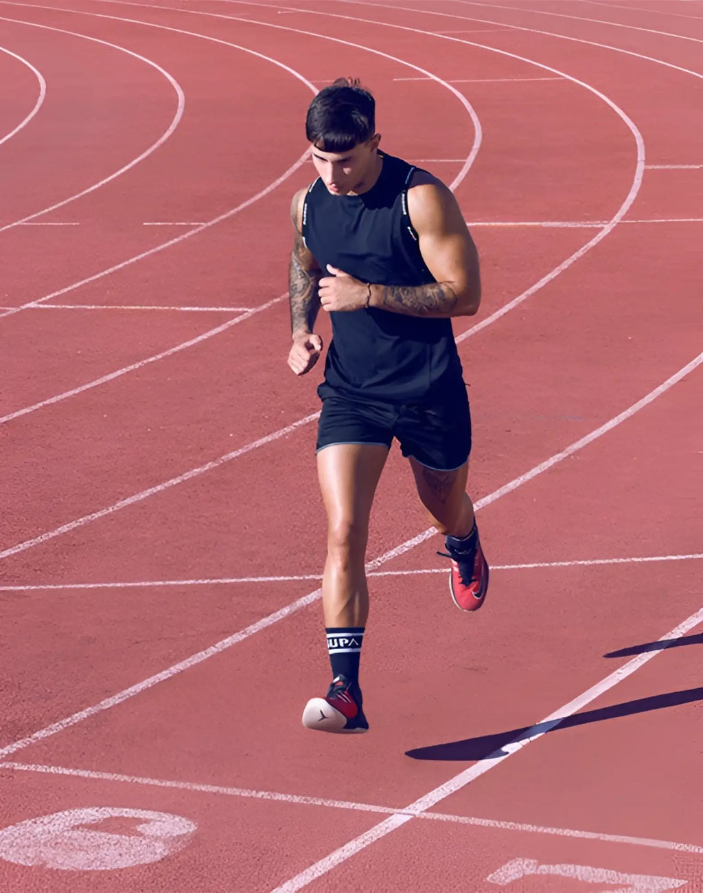 A man wearing black supawear spr racer shorts running on a red track with red and white sneakers visible branding