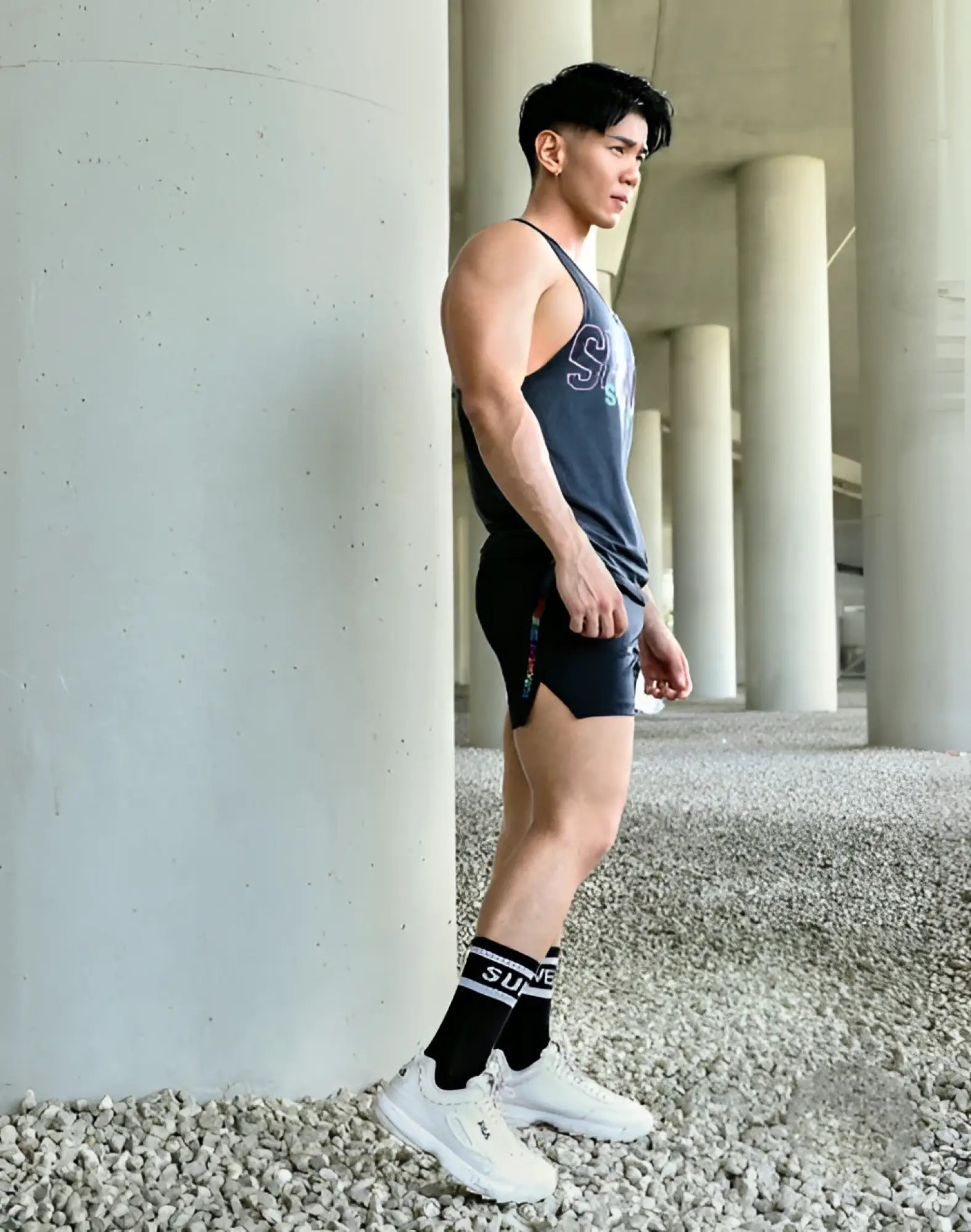 A man wearing supawear supa crew socks black os with dark gray tank top and black shorts with colorful side stripes
