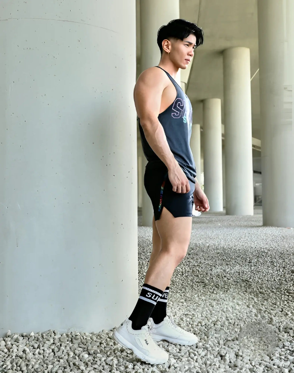 A man wearing supawear supa crew socks black os with dark gray tank top and black shorts with colorful side stripes