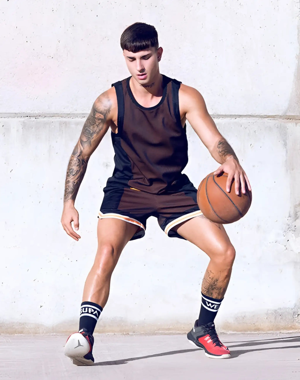A man dribbles an orange basketball wearing a black and brown athletic outfit with supawear swish mesh singlet neon orange