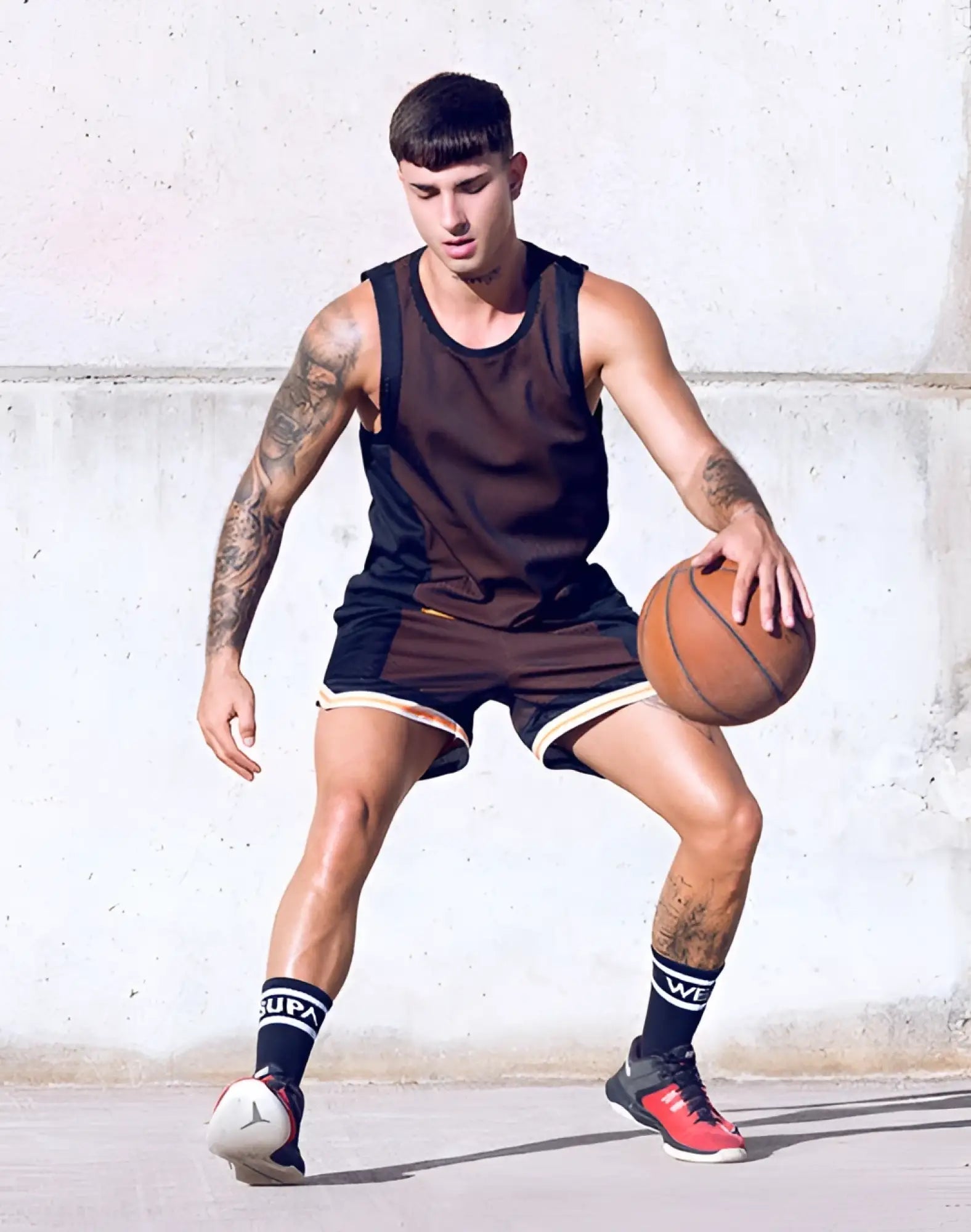 A man dribbles an orange basketball wearing a black and brown athletic outfit with supawear swish mesh singlet neon orange