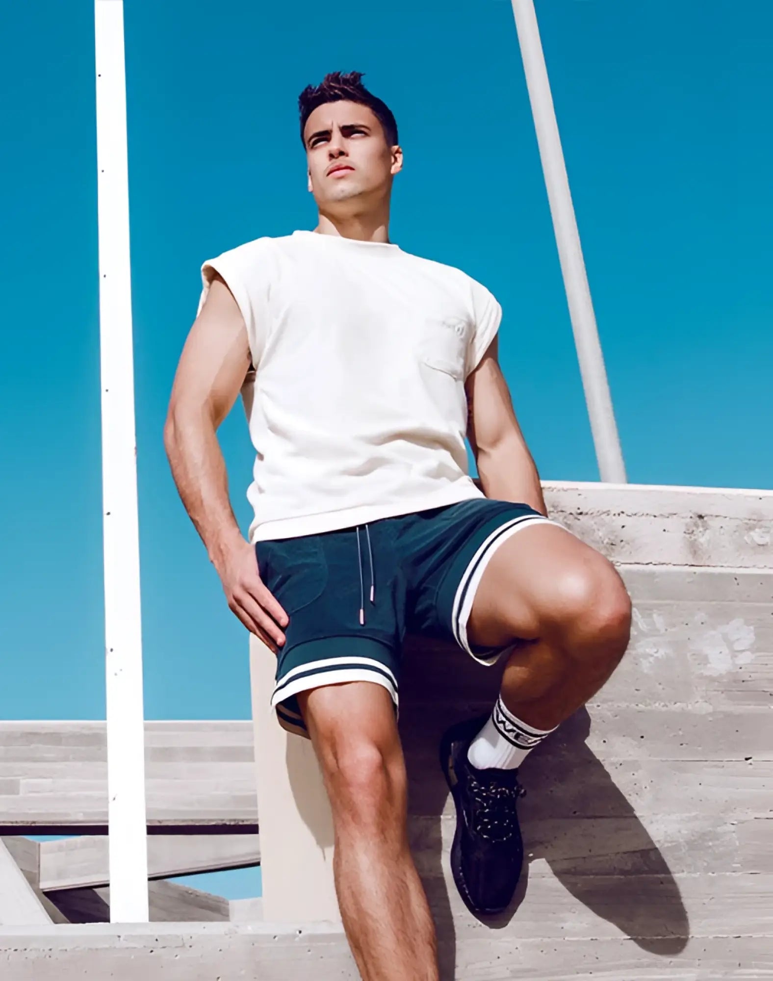 A man wearing a supawear terry towelling tank off white sleeveless t-shirt with chest pocket and dark green shorts with white stripes