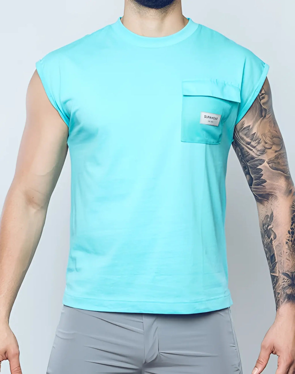A men’s light blue sleeveless supawear wide cut tank with a chest pocket and small white label in turquoise blue