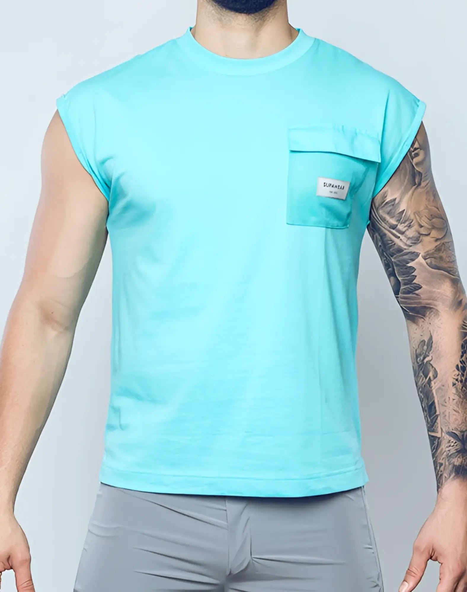 A men’s light blue sleeveless supawear wide cut tank with a chest pocket and small white label in turquoise blue