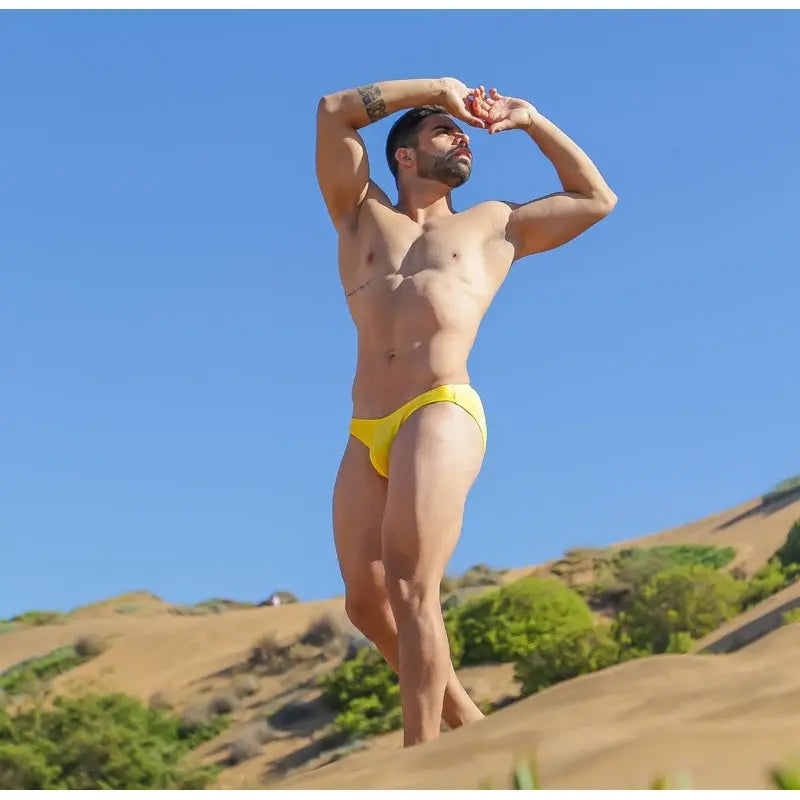 Model wearing yellow bikini swimwear by Arroyman showcasing a sleek design against a sunny outdoor backdrop.