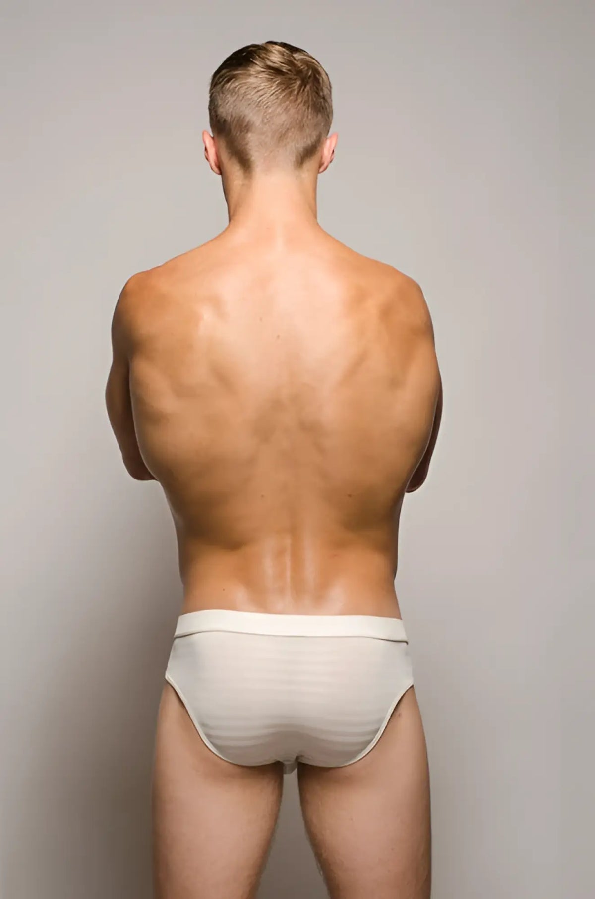 Back view of a man wearing white striped tartarus buckle brief underwear with a secure buckle design
