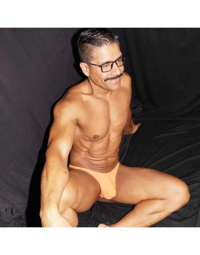 Model wearing Arroyman orange thong underwear showcasing a smooth fit and soft fabric against a dark background.