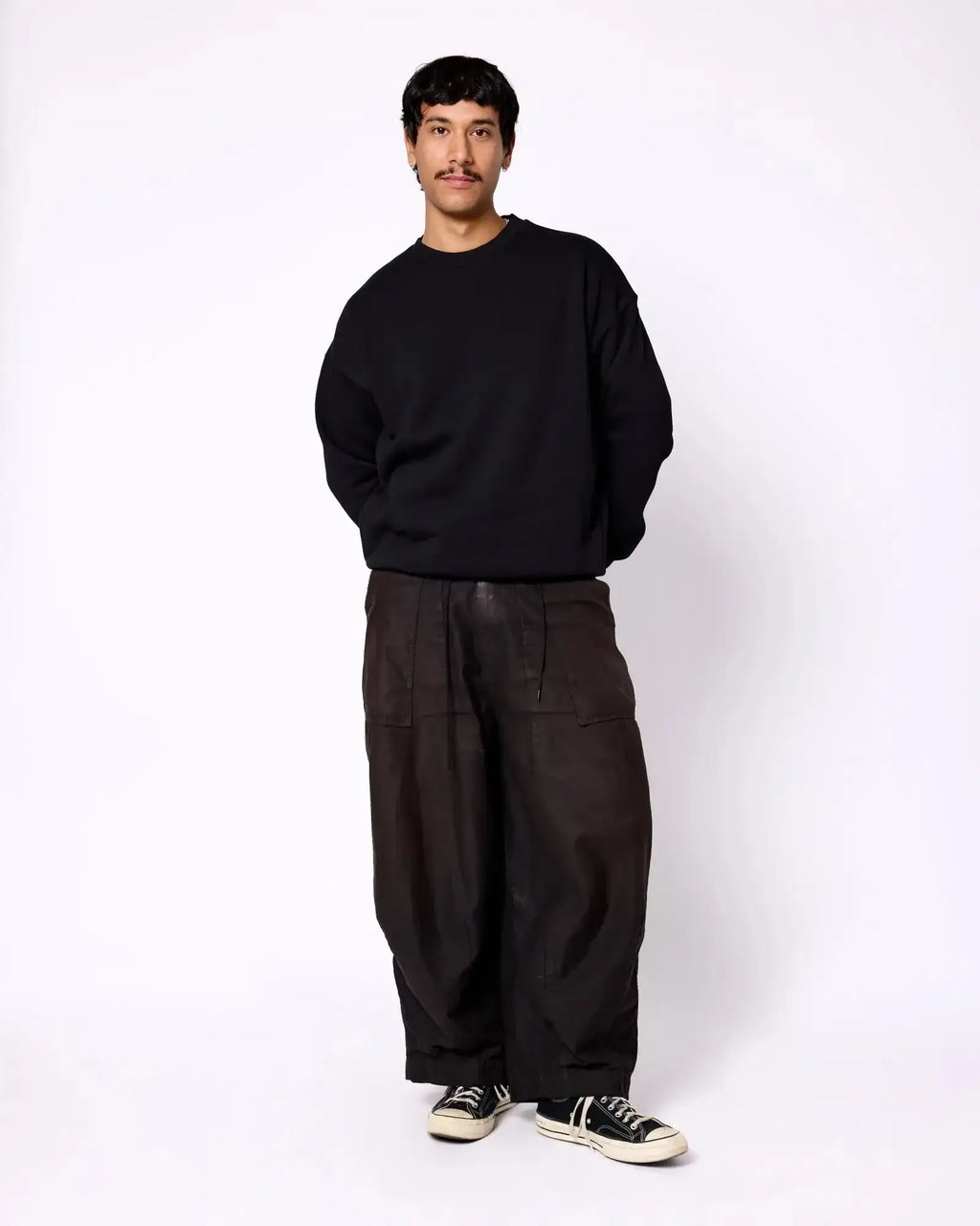 A man wearing a solid black crewneck sweatshirt with relaxed-fit, dark brown cargo pants and black sneakers.