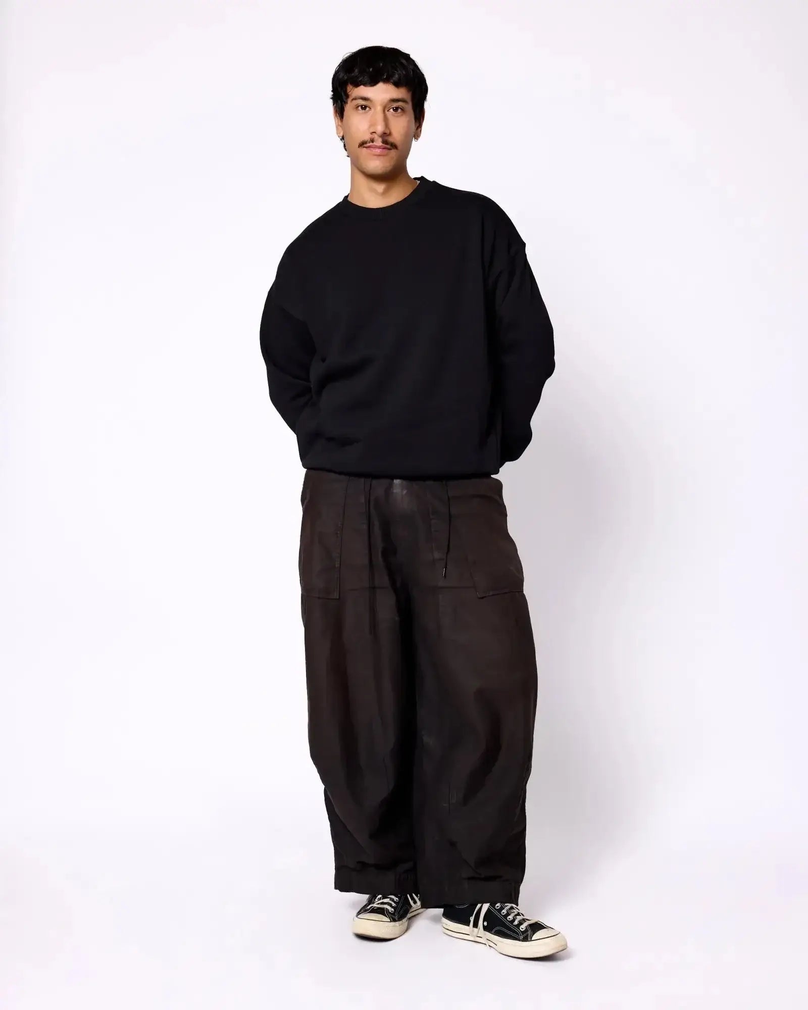 A man wearing a solid black crewneck sweatshirt with relaxed-fit, dark brown cargo pants and black sneakers.