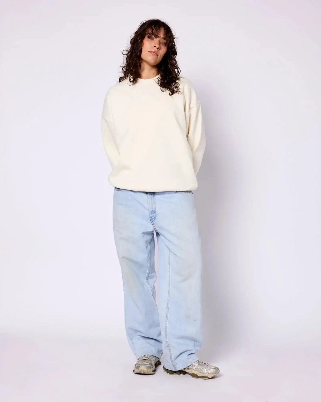 Model wearing a cream-colored, long-sleeve crewneck sweatshirt with dropped shoulders and a relaxed fit.
