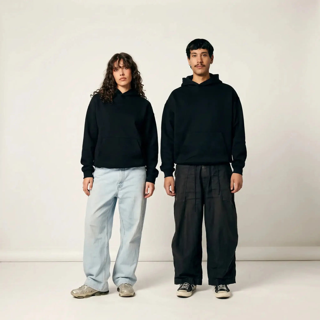 Man and woman wearing black Thread Lab Core Hoodies, styled with wide-leg trousers, clean studio editorial shot.