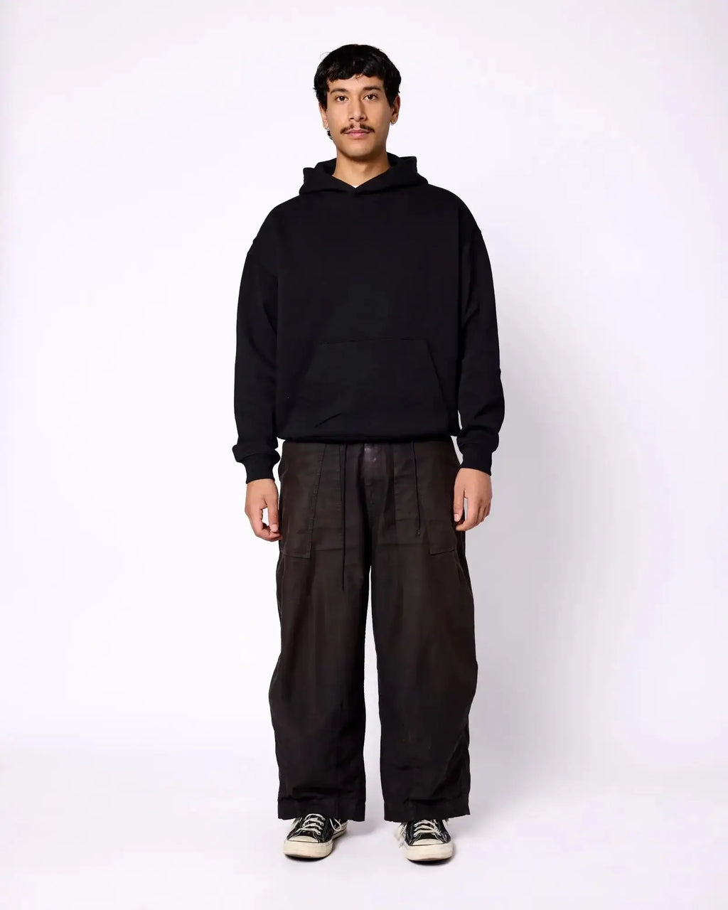 Model wearing a solid black, relaxed-fit pullover hoodie with a spacious front kangaroo pocket.