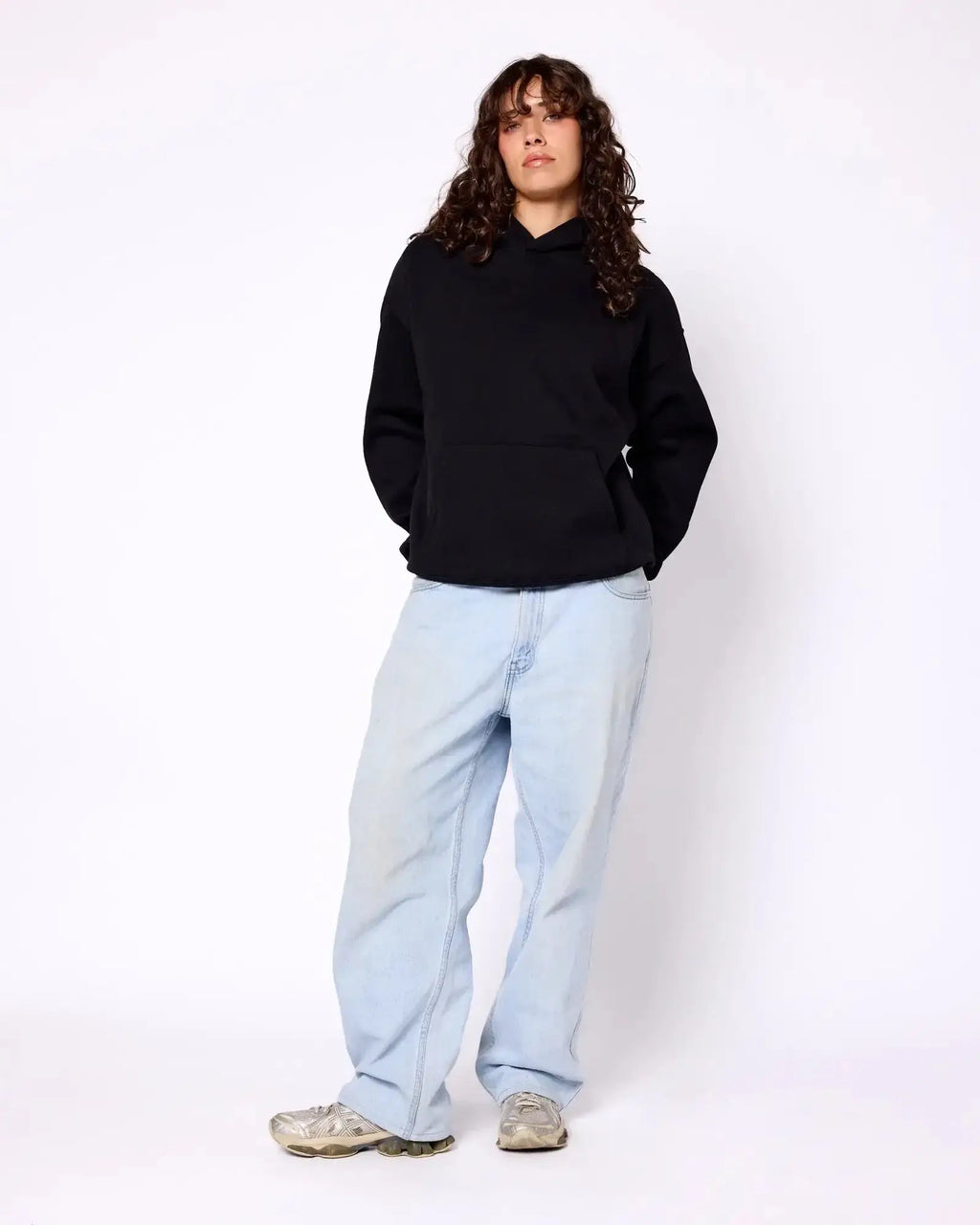 Model wearing a black, long-sleeve Core Hoodie with a front kangaroo pocket, paired with light-wash baggy jeans.