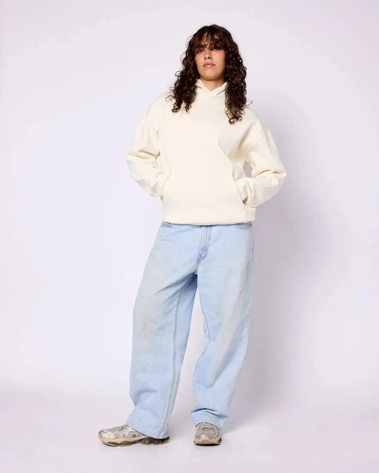 Model wearing an oversized, cream-colored Core Hoodie with a front kangaroo pocket, paired with light-wash baggy jeans.