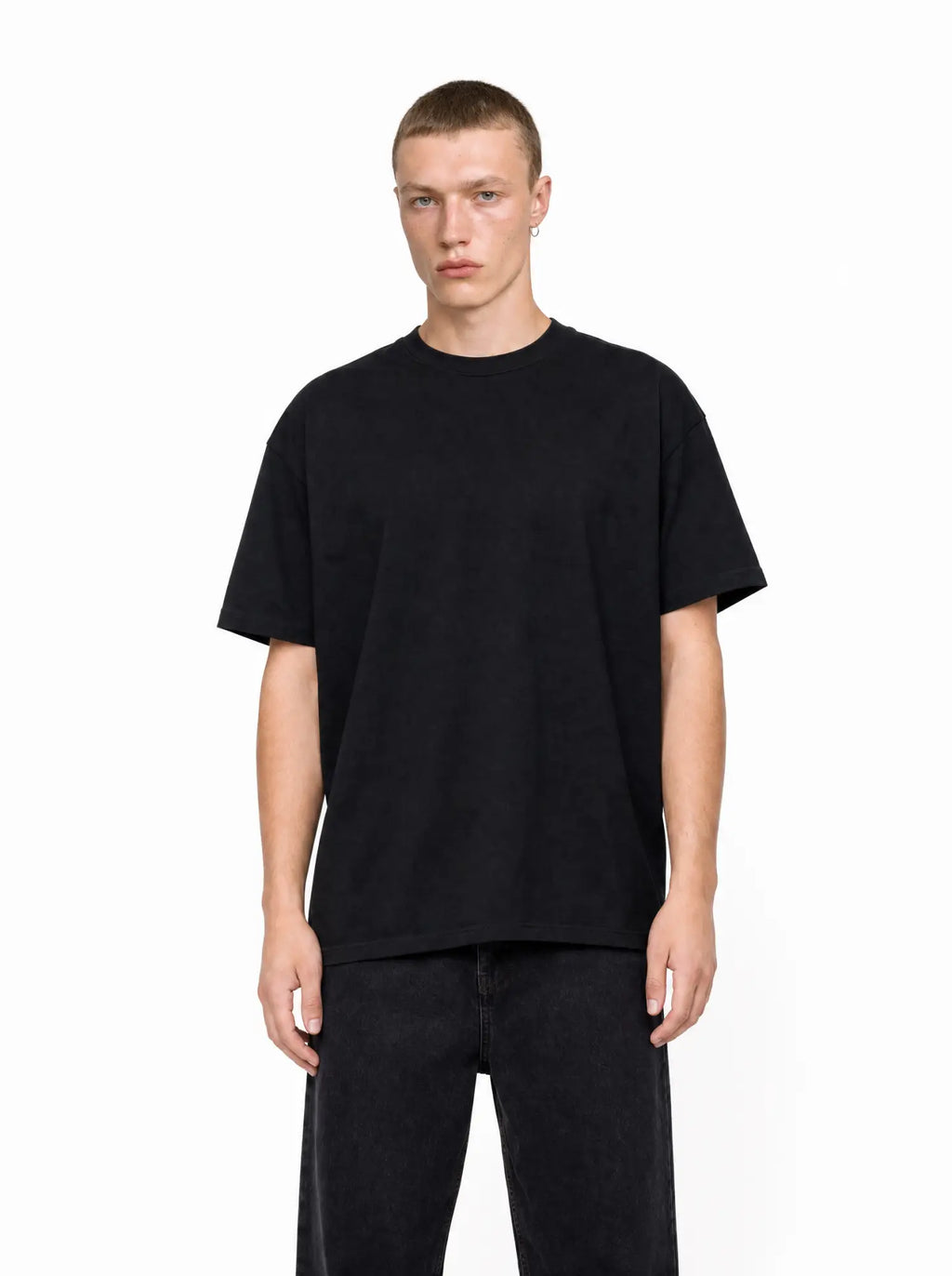 A man wearing a black, loose-fit Core Tee with a crew neck and dropped shoulders, styled with dark jeans.