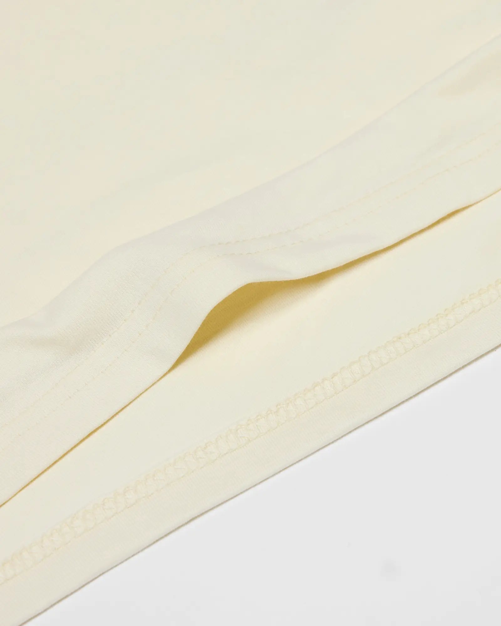 Close-up of a cream-colored Core Tee showing the smooth fabric texture and stitched hem detail.