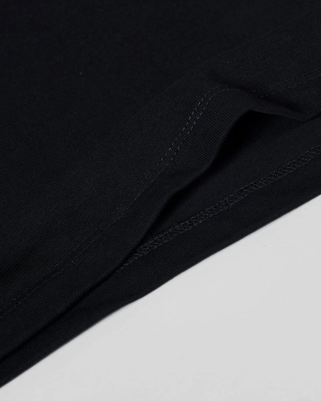 Close-up of a black premium tee showing the high-quality fabric texture and detailed stitched hem.