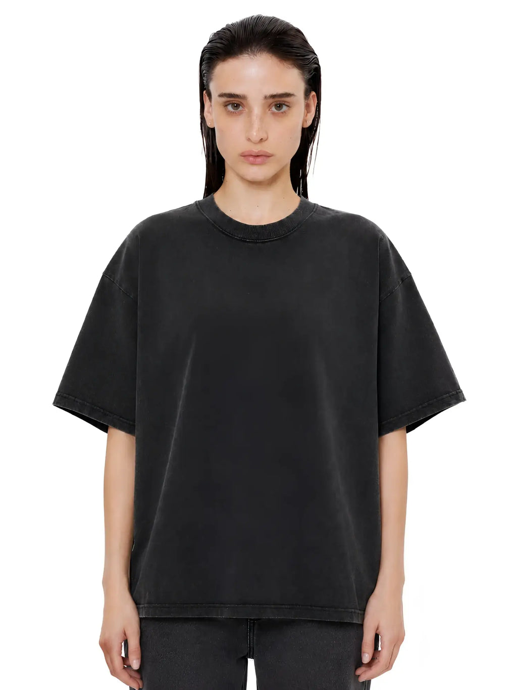 Model wearing an oversized, vintage-wash charcoal black crewneck t-shirt with drop shoulders and a ribbed collar.