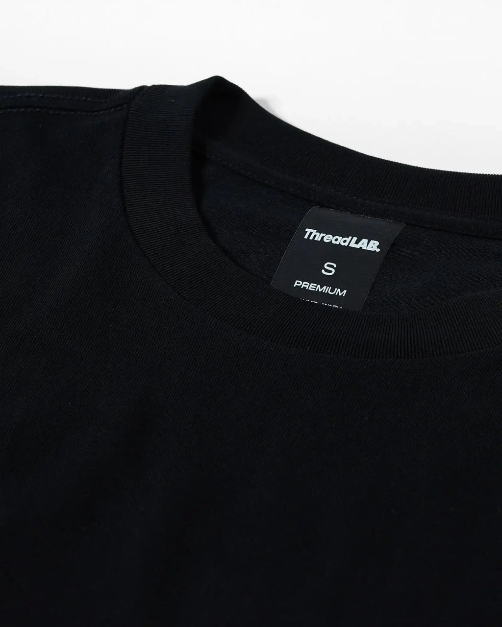 Close-up of a black crew neck t-shirt with a ThreadLAB Premium size small tag inside the collar.