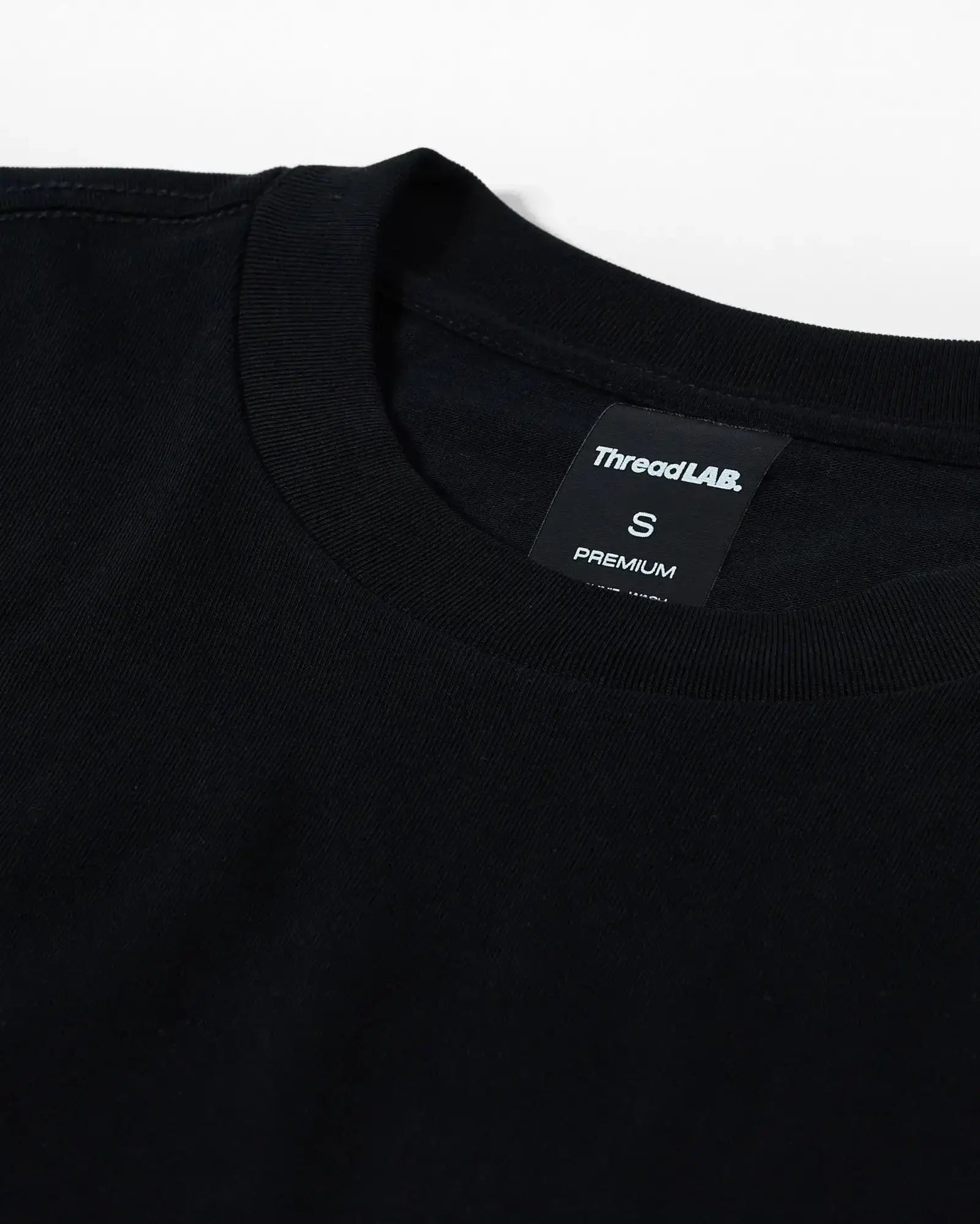 Close-up of a black crew neck t-shirt with a ThreadLAB Premium size small tag inside the collar.