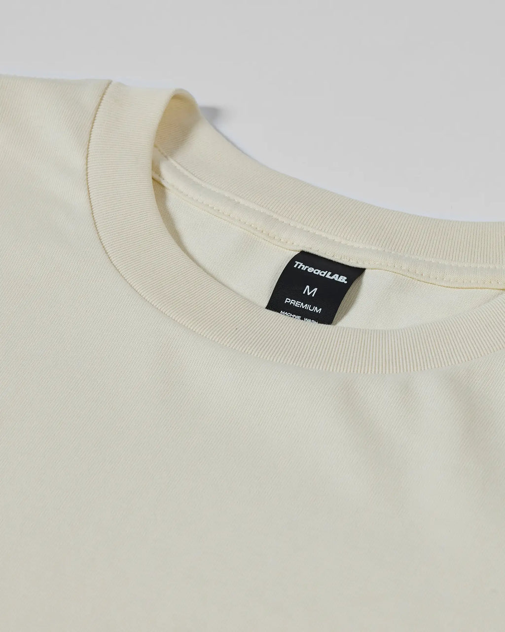 Close-up of a cream-colored crew neck T-shirt with a ThreadLAB tag indicating size M.
