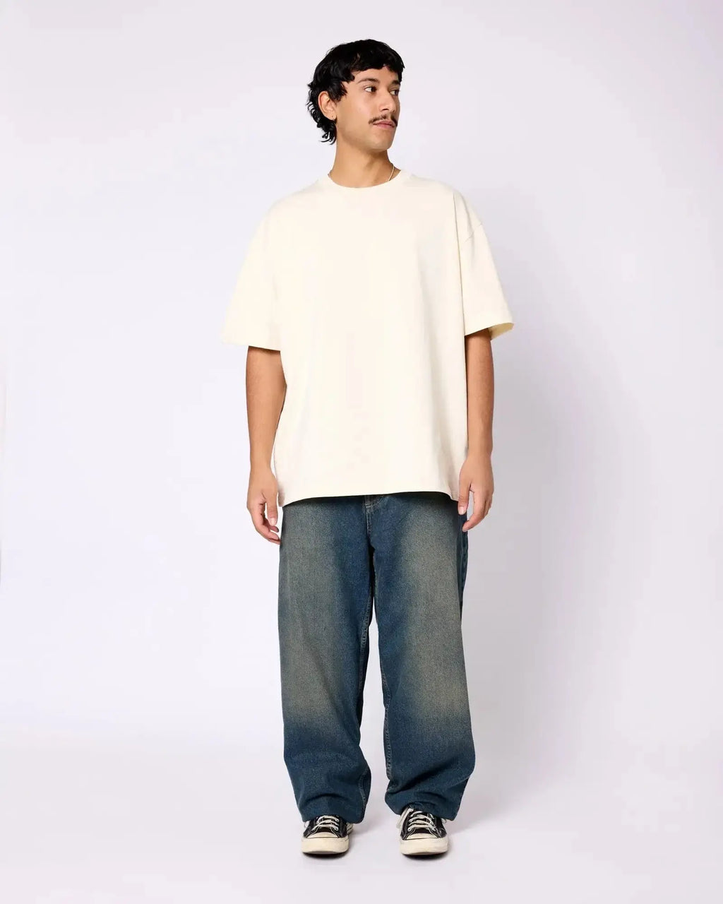 A man wearing an oversized, cream-colored premium crewneck tee with short sleeves against a white background.