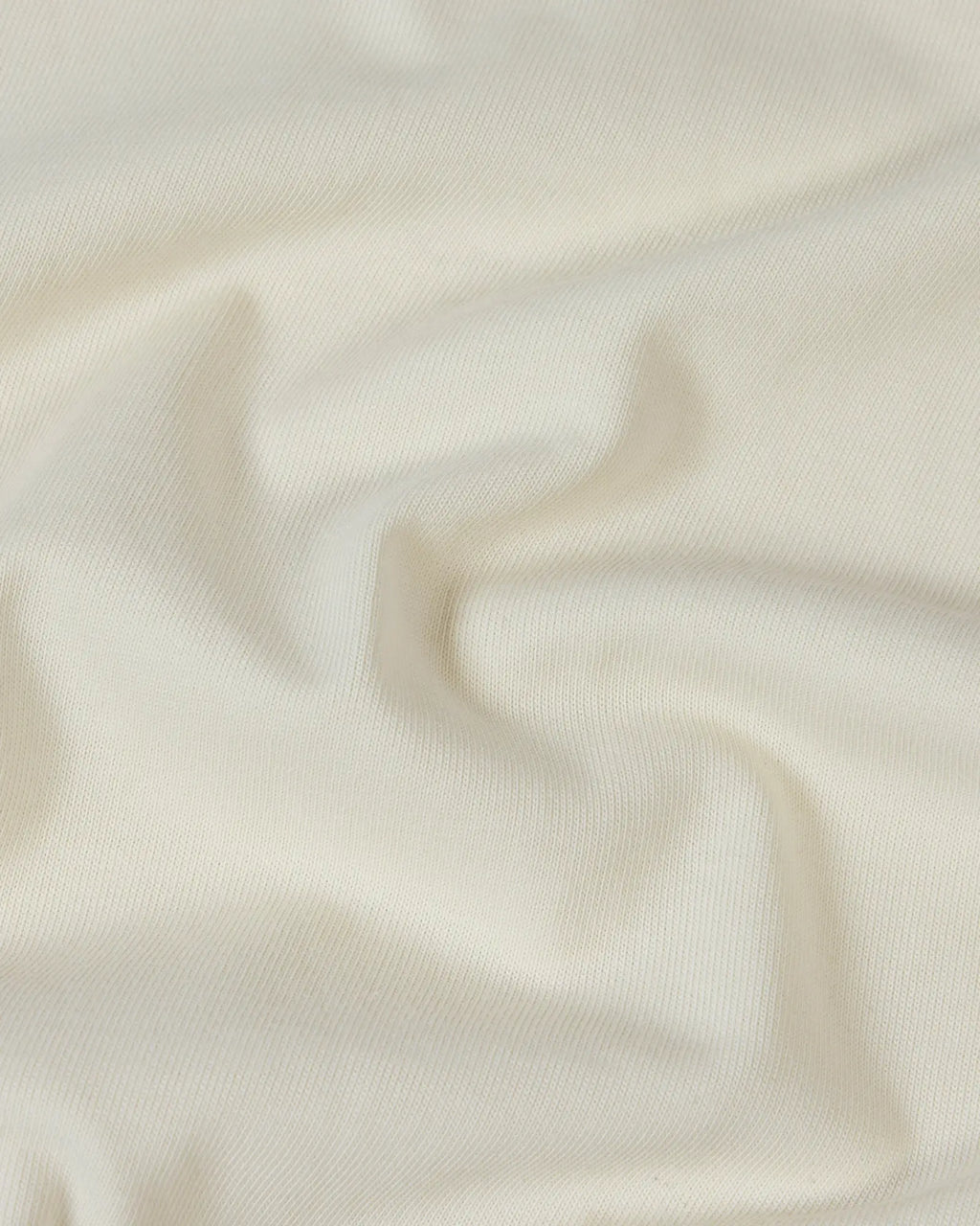 Close-up of soft, off-white premium cotton fabric with gentle folds and a smooth, high-quality knit texture.