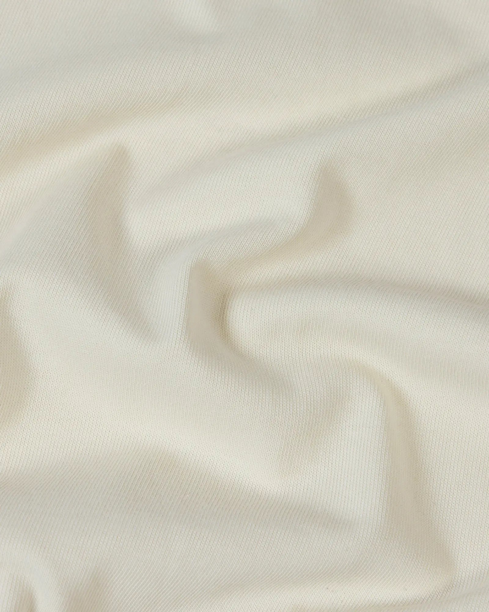 Close-up of soft, off-white premium cotton fabric with gentle folds and a smooth, high-quality knit texture.