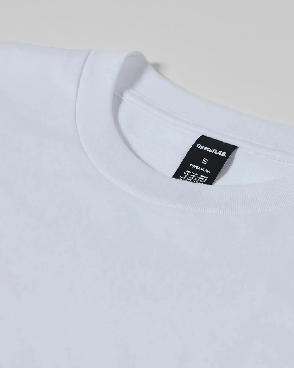Close-up of a plain white premium crew neck t-shirt with a black ThreadLAB neck label indicating size small.