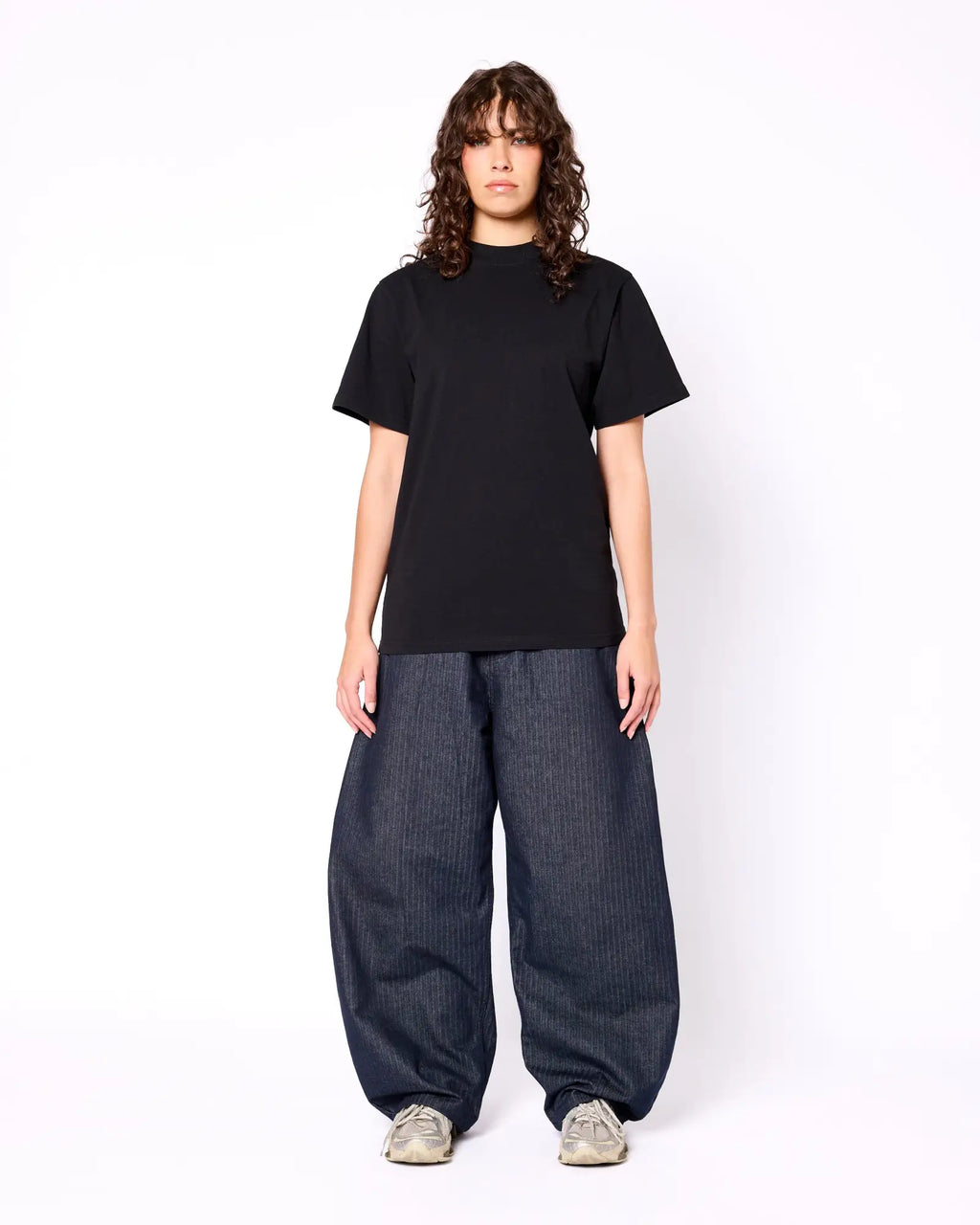Model wearing a black, heavyweight mock-neck short-sleeve tee paired with baggy, pinstriped navy trousers.