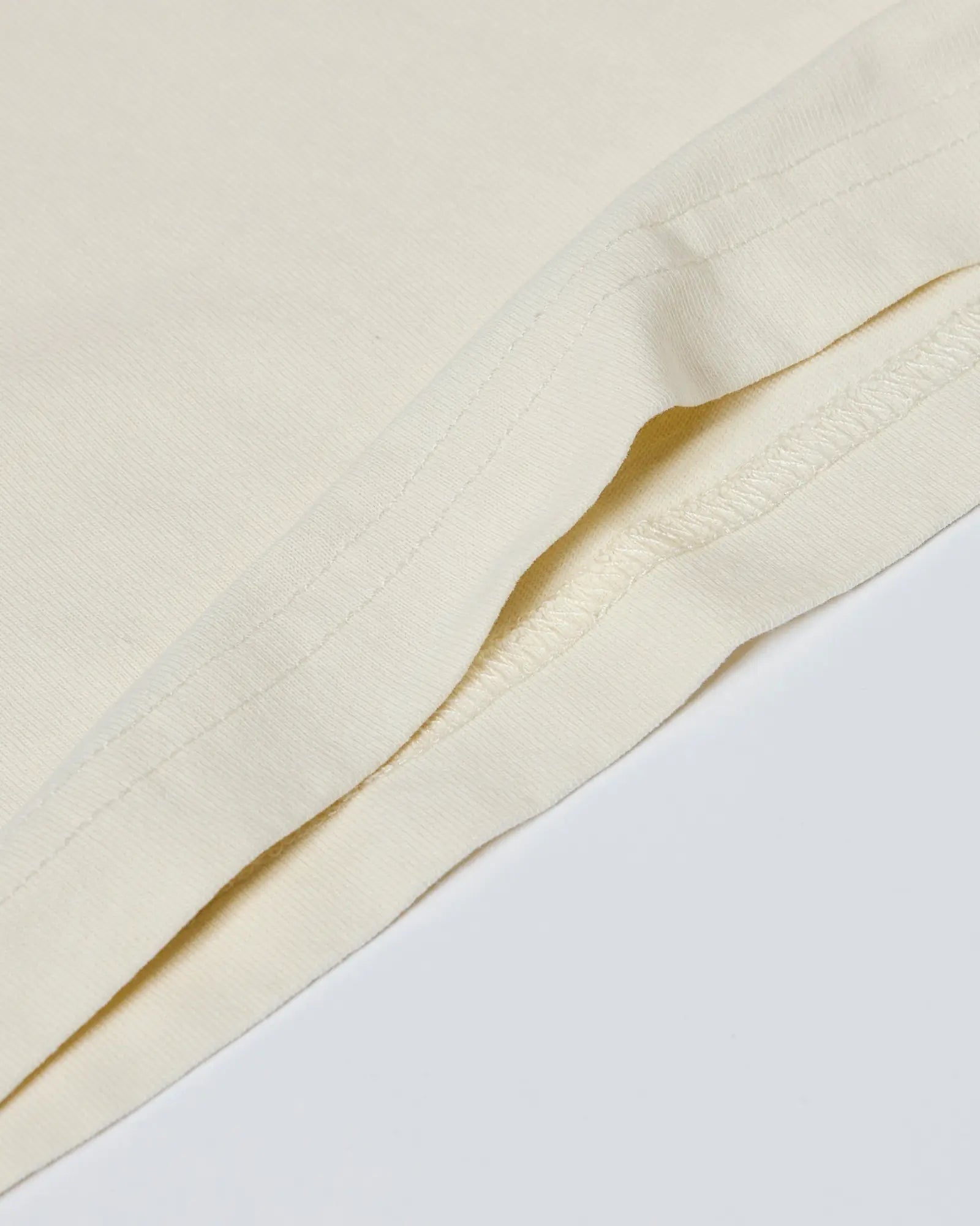 Close-up of a cream-colored t-shirt showing smooth fabric texture and durable double-needle hem stitching.