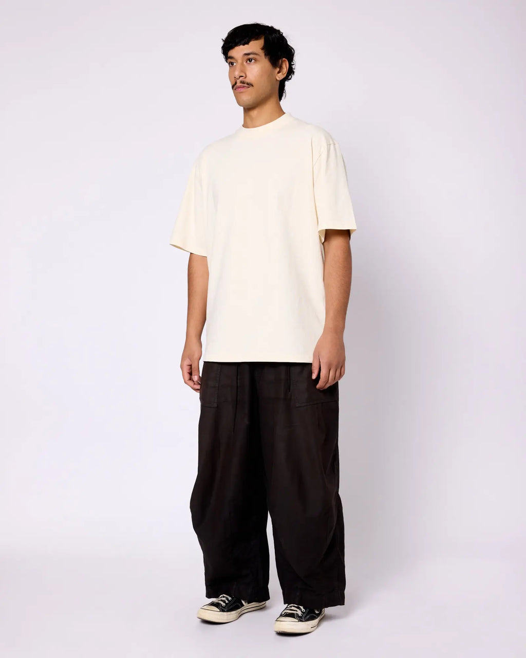 A man wears a cream-colored, heavyweight crewneck tee with a boxy, relaxed fit.