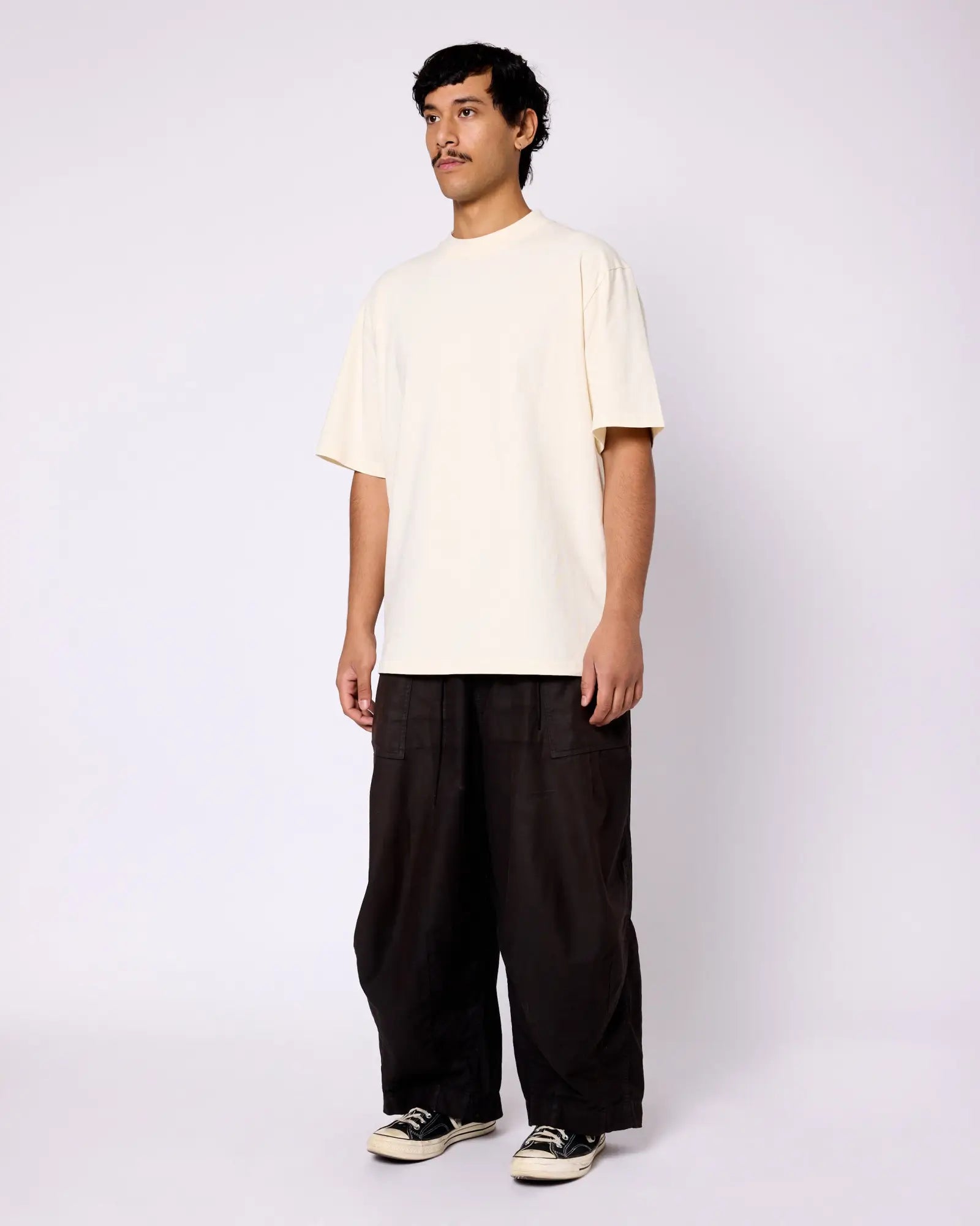 A man wears a cream-colored, heavyweight crewneck tee with a boxy, relaxed fit.