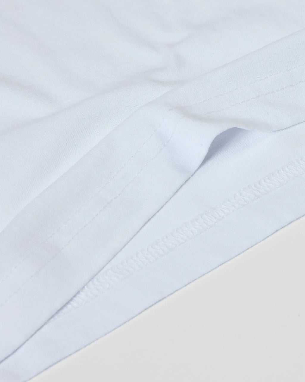 Close-up of a plain white Superior Tee showing high-quality fabric texture and detailed double-needle hem stitching.