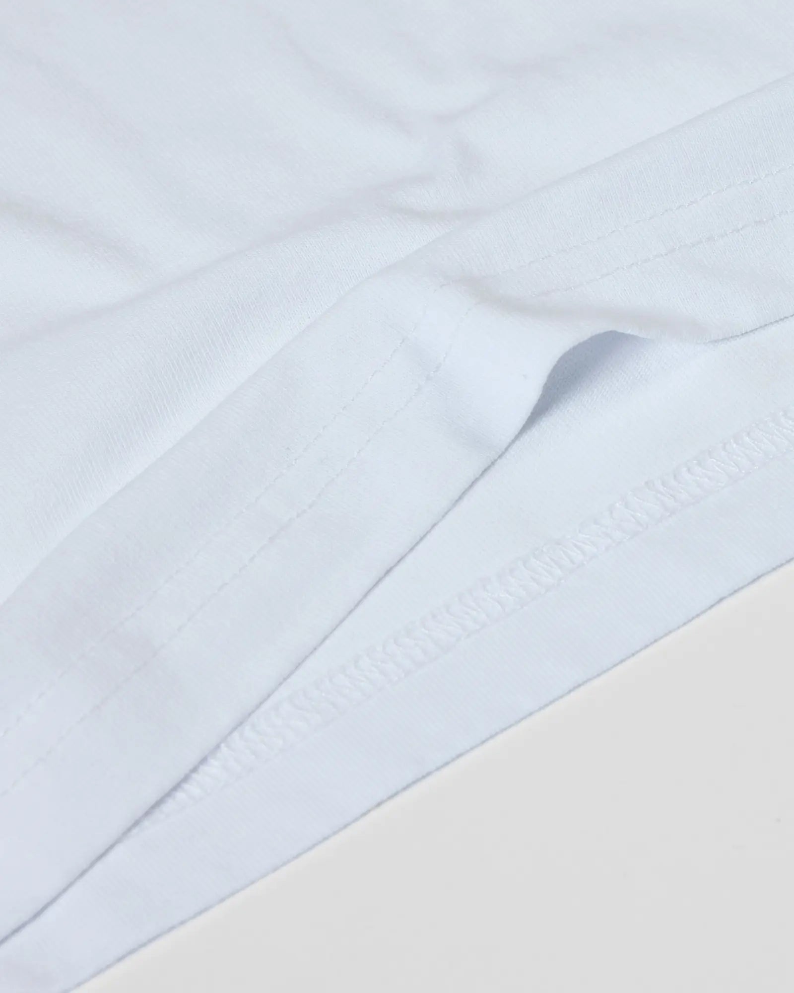 Close-up of a plain white Superior Tee showing high-quality fabric texture and detailed double-needle hem stitching.