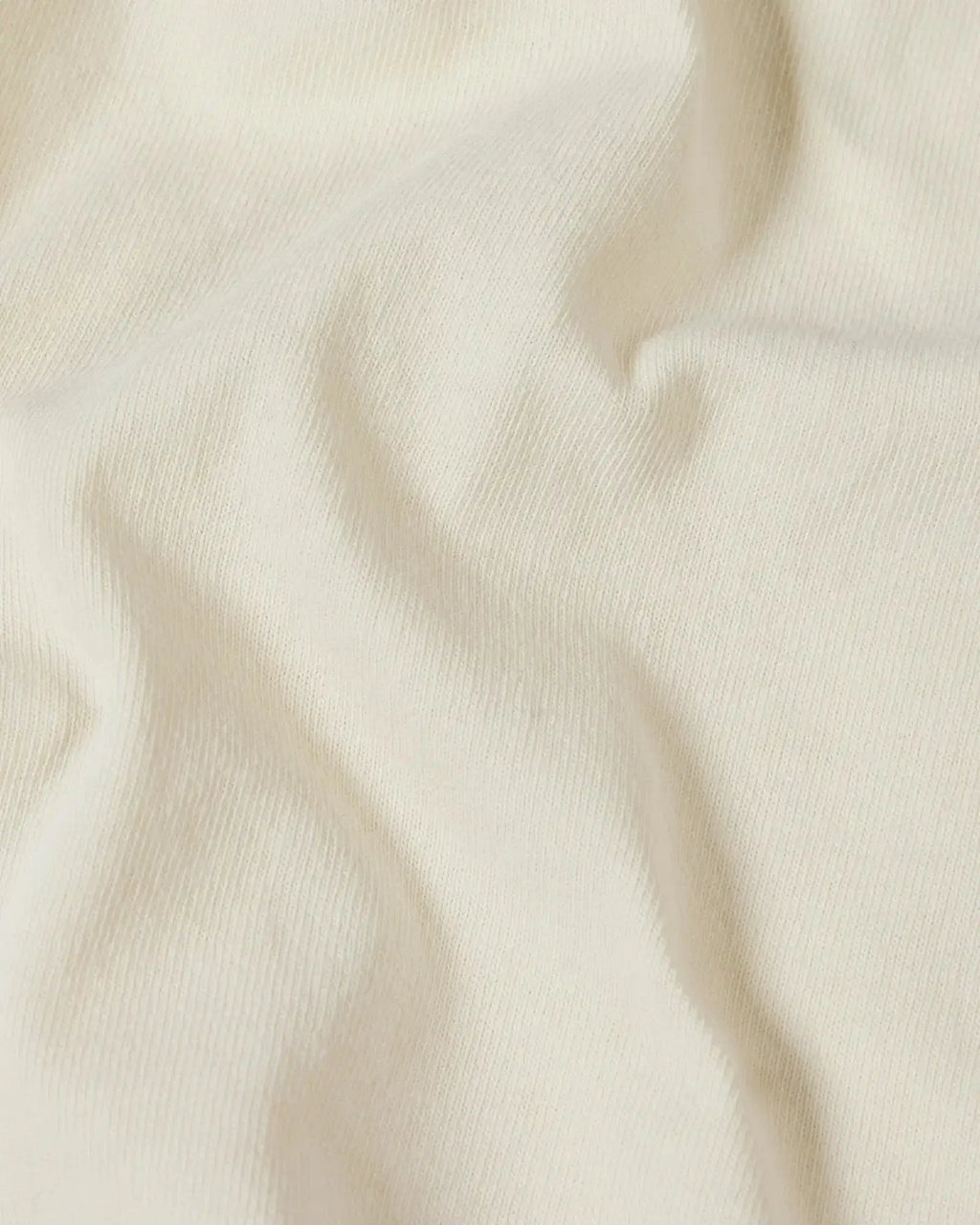 Close-up of a soft, off-white cotton Superior Tee fabric with gentle folds highlighting the knit texture.
