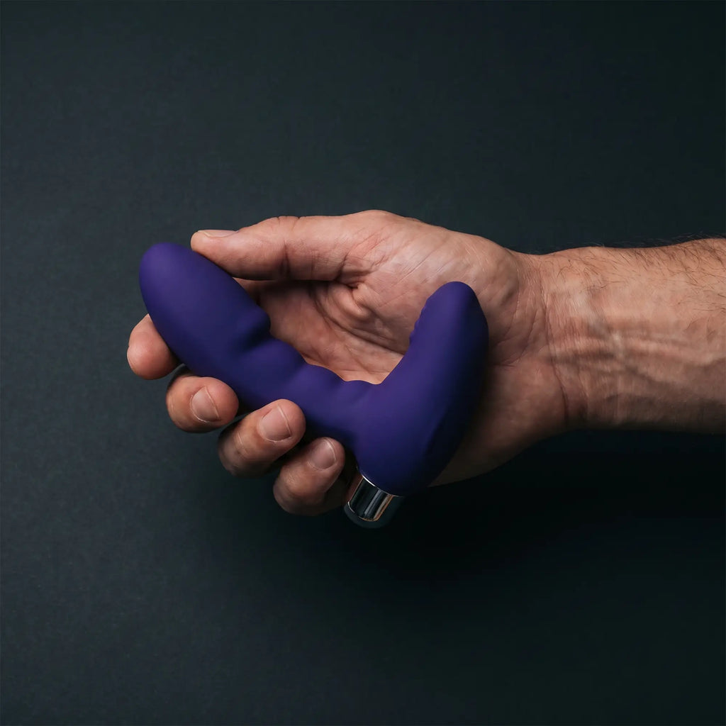 Man's hand holding the ToDo Bruman deep purple silicone prostate stimulator on dark matte surface — lifestyle shot